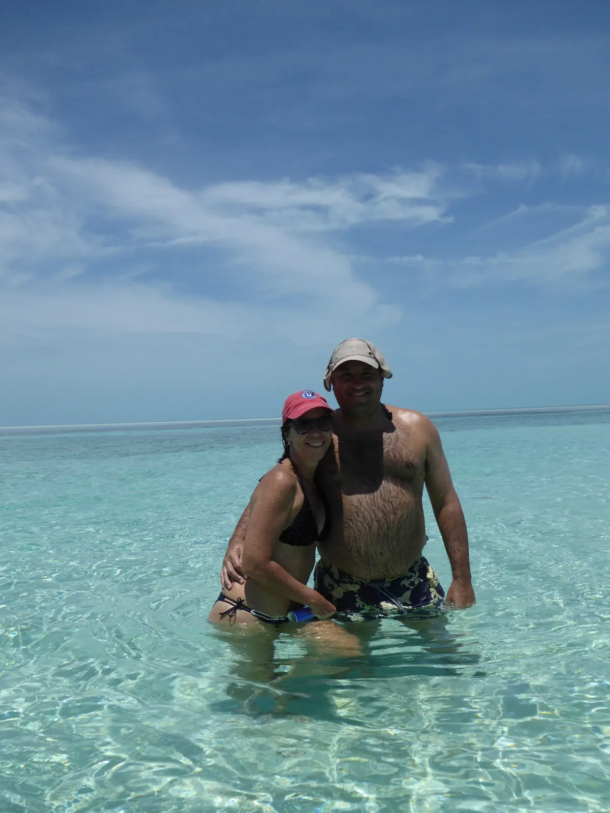 El autor y Dolores, abrazados, de pie en un agua transparente que les llega a la cintura; detrás, el mar turquesa hasta el horizonte bajo un cielo azul con nubes altas
